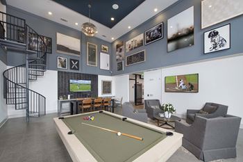 A billiard table is in the middle of a room with a spiral staircase.